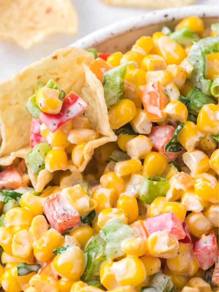 A corn salad with a chip inside of it using it as a dip.