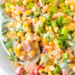 A bowl with corn salad inside of it covered in ranch dressing and seasonings.