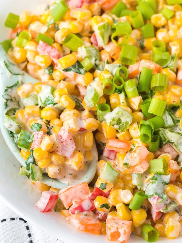 A bowl with corn salad inside of it covered in ranch dressing and seasonings. 