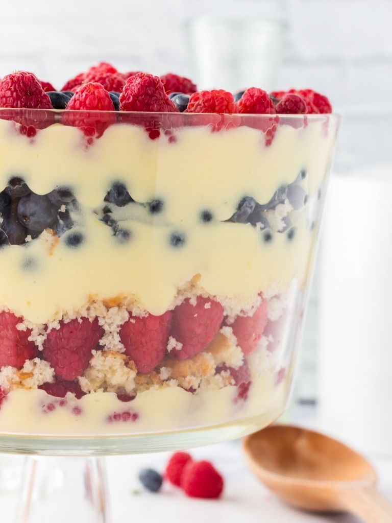 A close up view of a glass trifle dish with layers of cake, pudding, and berries inside of it. 