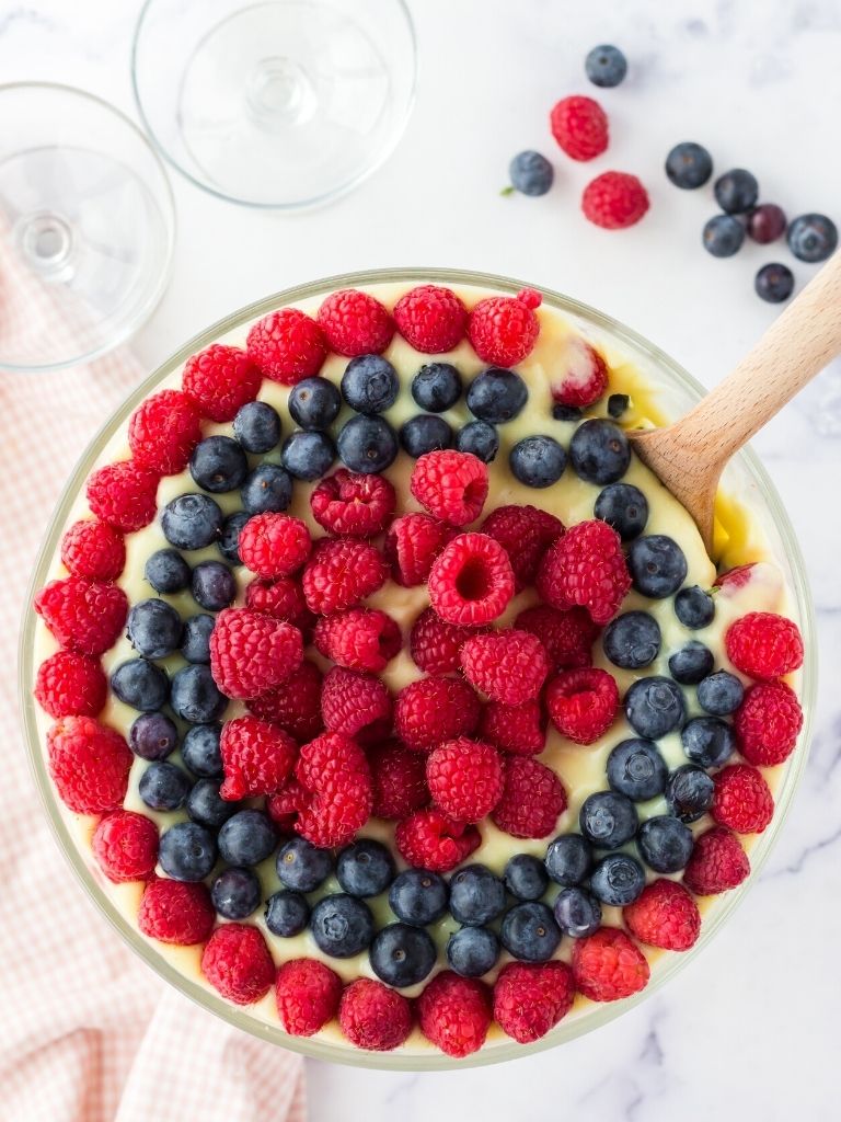 Trifle with a wooden spoon inside of it and fresh berries on top.