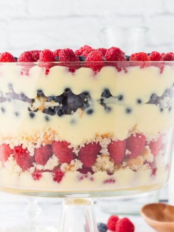A glass trifle dish layered with fresh berries, instant pudding, and cake chunks.