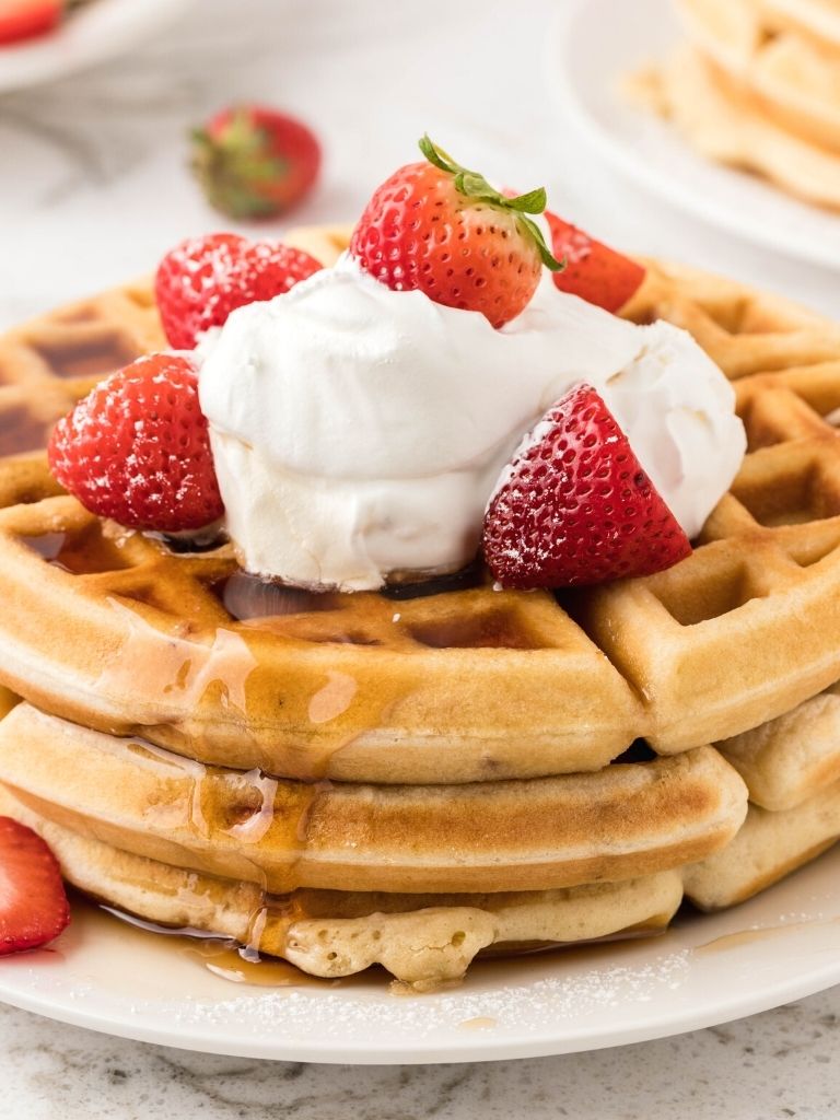 Stack of waffles topped with whipped cream and fresh strawberries. 