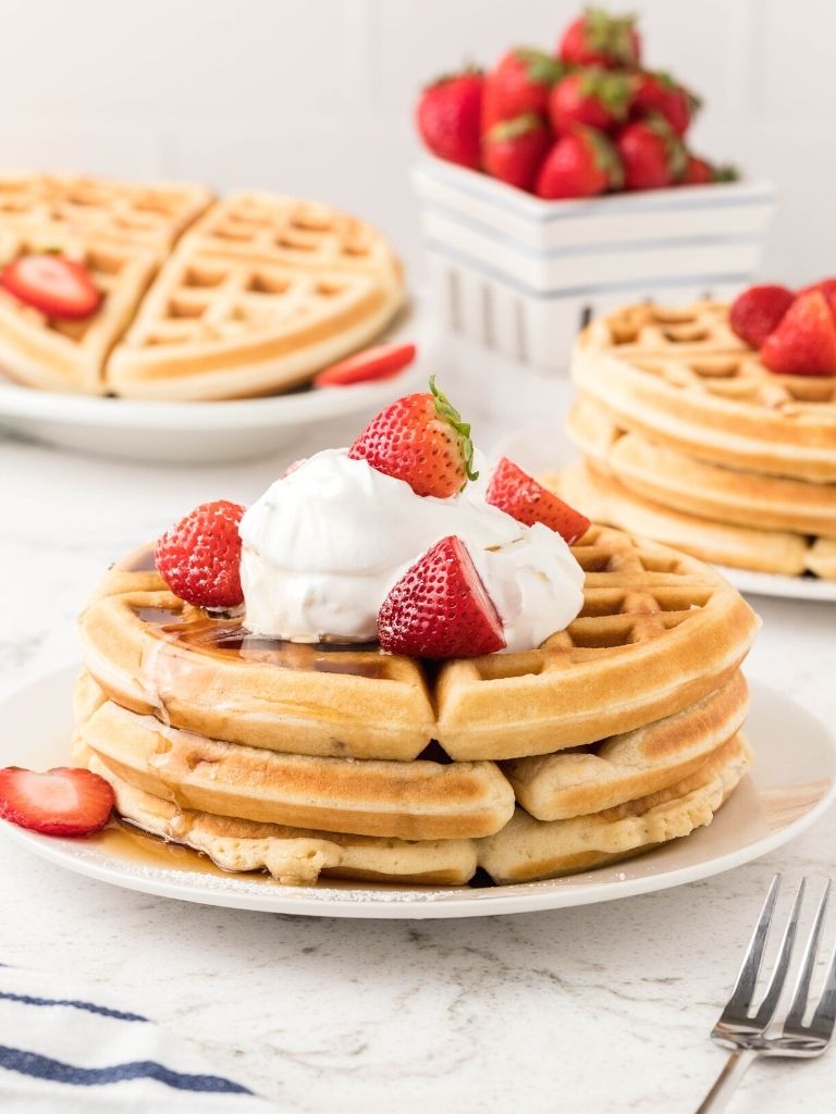 Stack of strawberry waffles on a white plate with plates of waffles in the background.