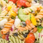 Close up shot of a pasta salad on a white plate with a silver fork by it.