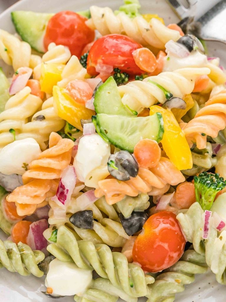 Close up shot of a pasta salad on a white plate with a silver fork by it. 