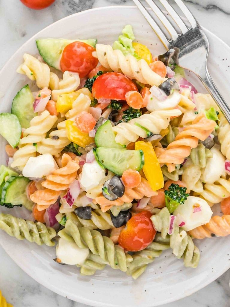 A white plate with tri color pasta salad on it and a silver fork on the side. 