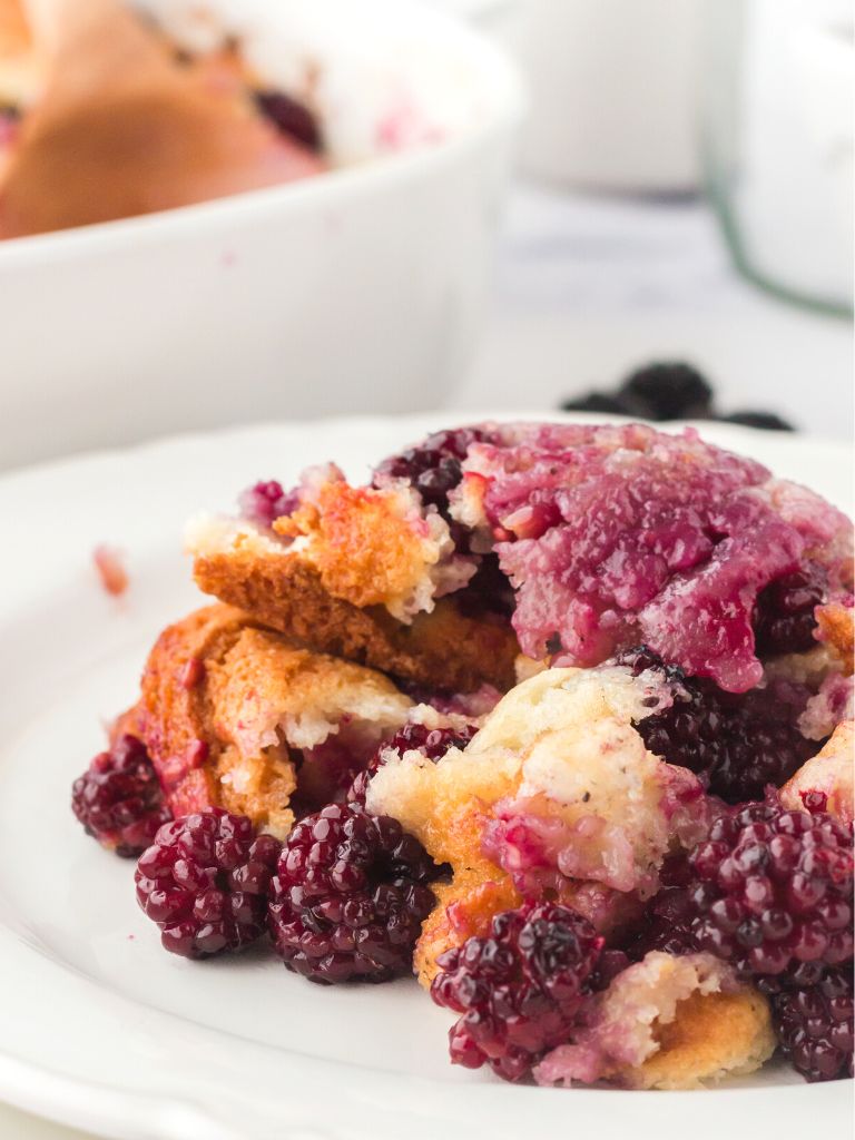 Cobbler with blackberries sitting on top of a stack of white plates. 