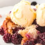 A white plate with blackberry cobbler on it and topped with a scoop of vanilla ice cream on top.