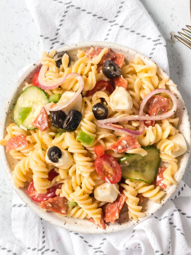Overhead picture of a bowl of pasta salad on top of a white and blue linen cloth. 