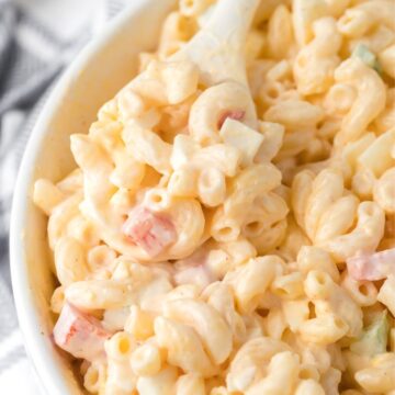 White bowl with creamy macaroni salad inside of it and a white spoon.
