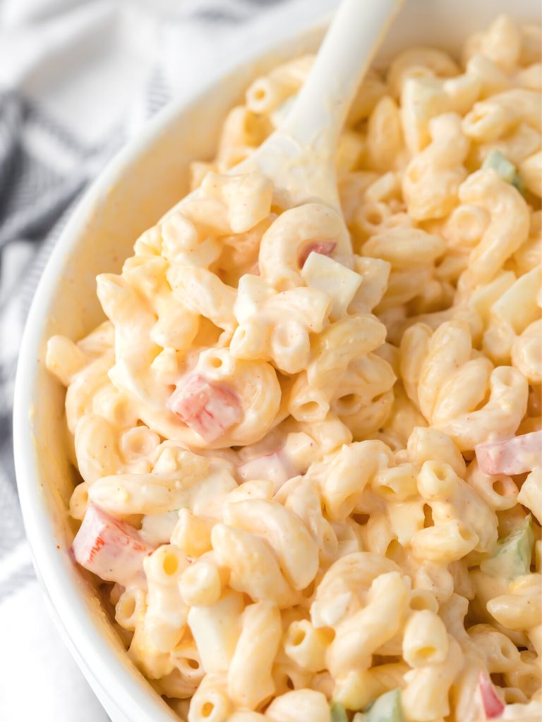 White bowl with creamy macaroni salad inside of it and a white spoon. 