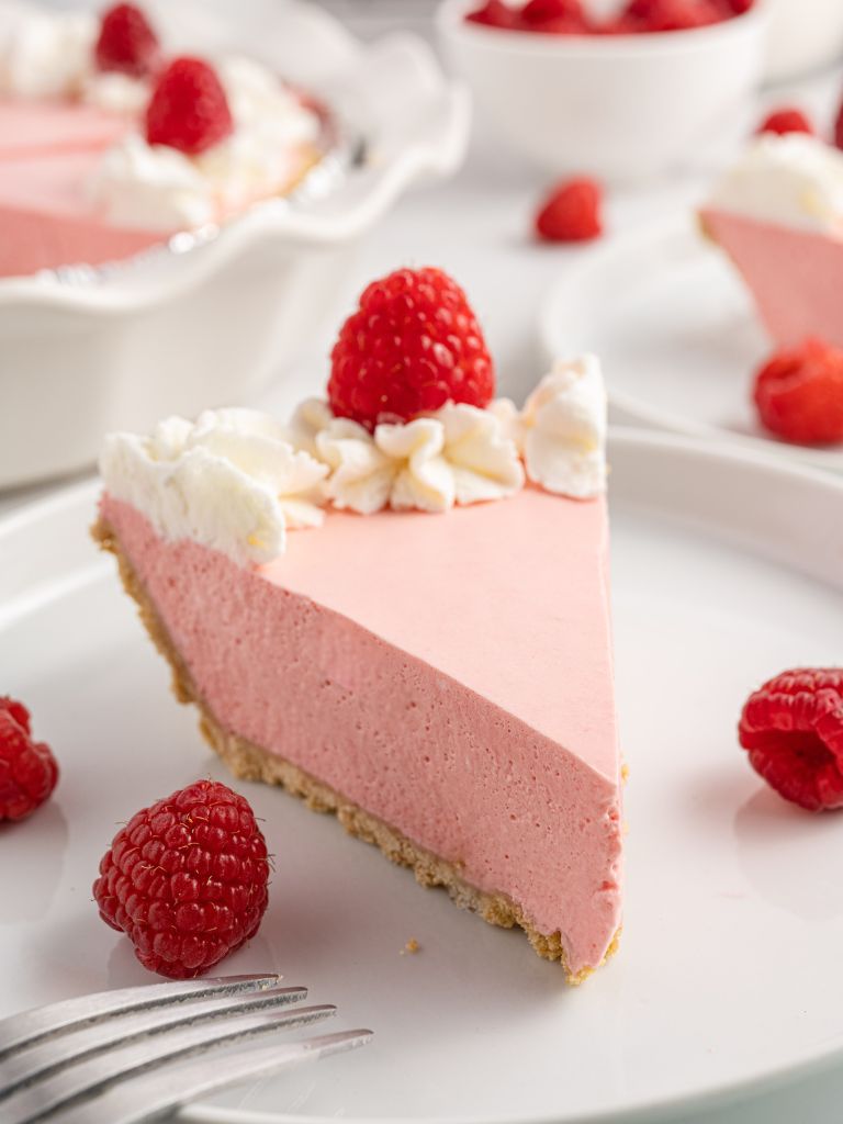 A slice of creamy pie topped with raspberries and whipped cream. 