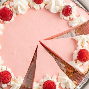 Overhead photo of a pink pie inside a crust topped with whipped cream and raspberries.