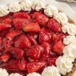 Side view of a strawberry pie topped with whipped cream.