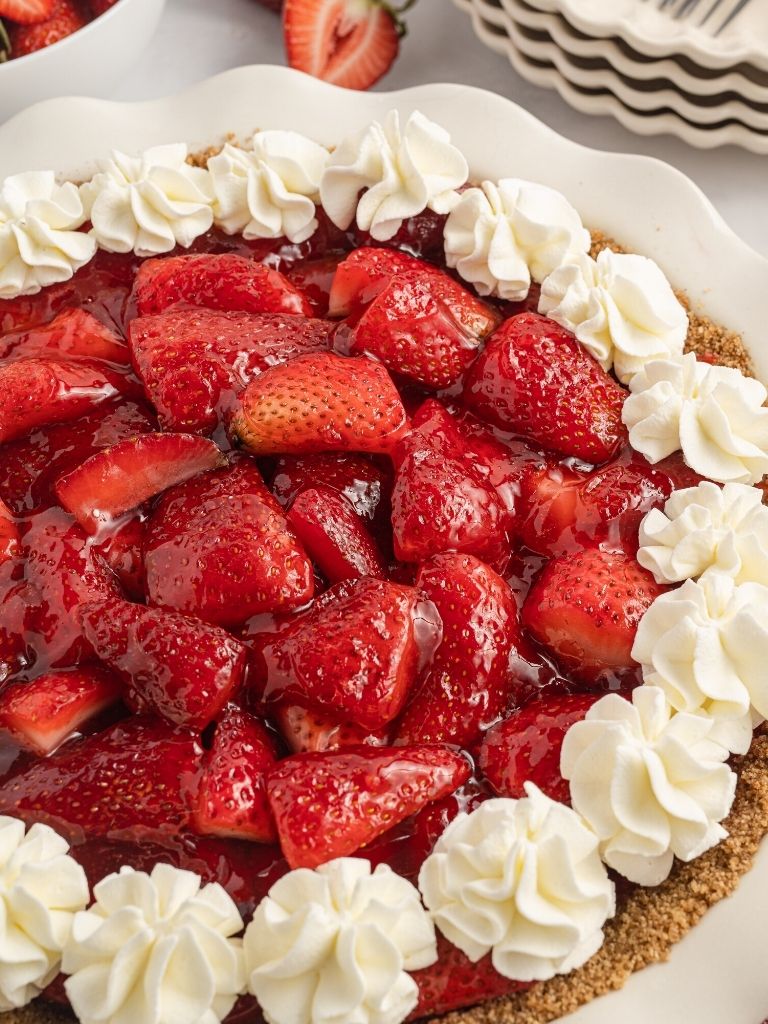 Side view of a strawberry pie topped with whipped cream.