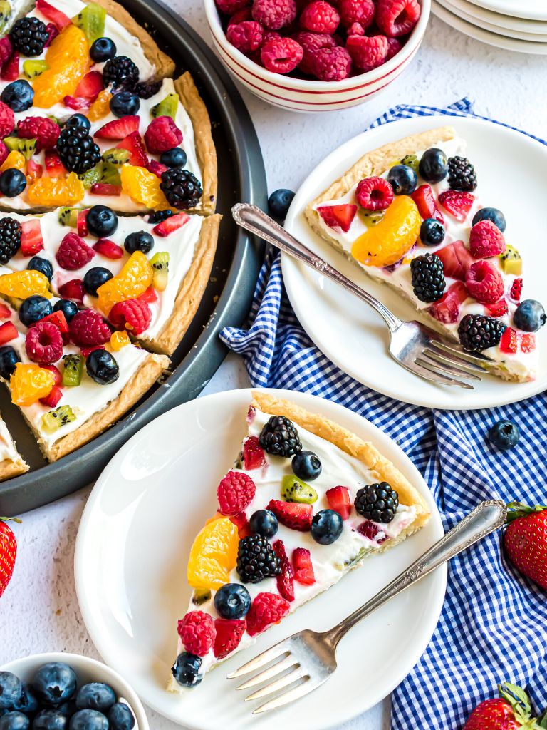 Overhead shot of a fruit dessert pizza with some slices on plated with forks. 