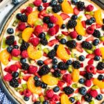 A sugar cookie crust with cream cheese and topped with fruit inside a pizza pan.