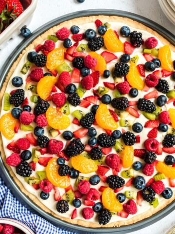 A sugar cookie crust with cream cheese and topped with fruit inside a pizza pan.