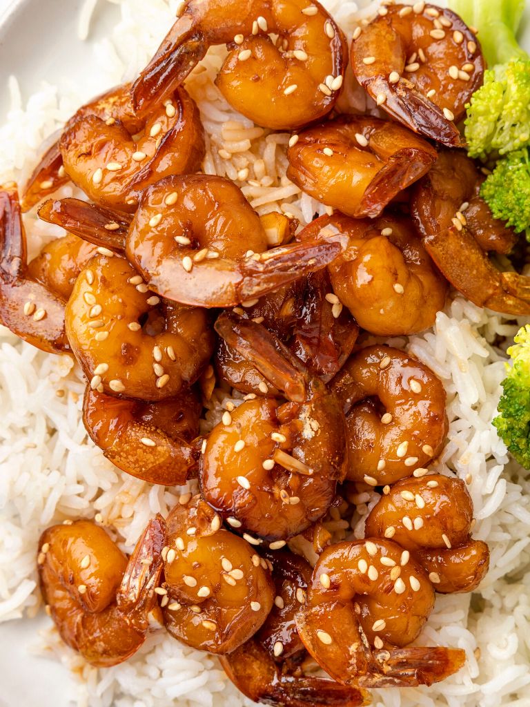 A white plate with broccoli and white rice topped with marinated shrimp in a honey garlic soy sauce marinade. 