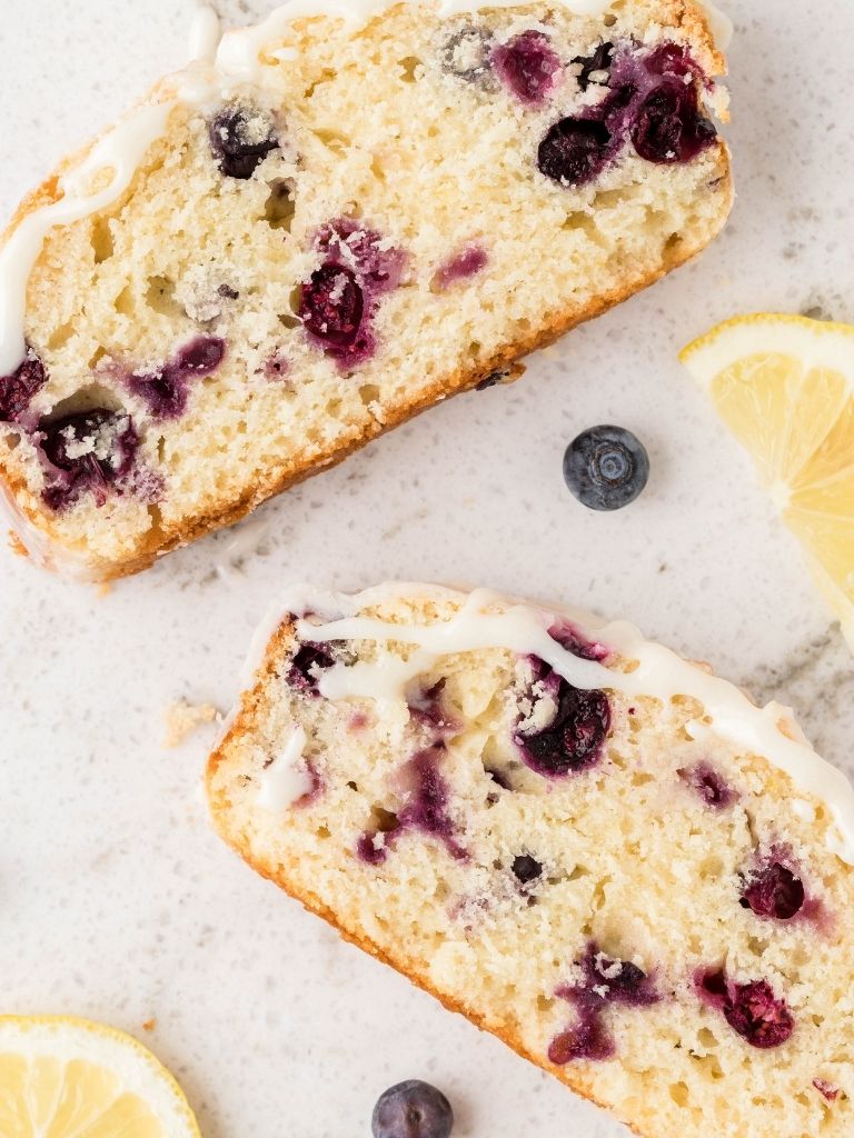 Two slices of lemon blueberry bread with blueberries and lemon slices on the side. 