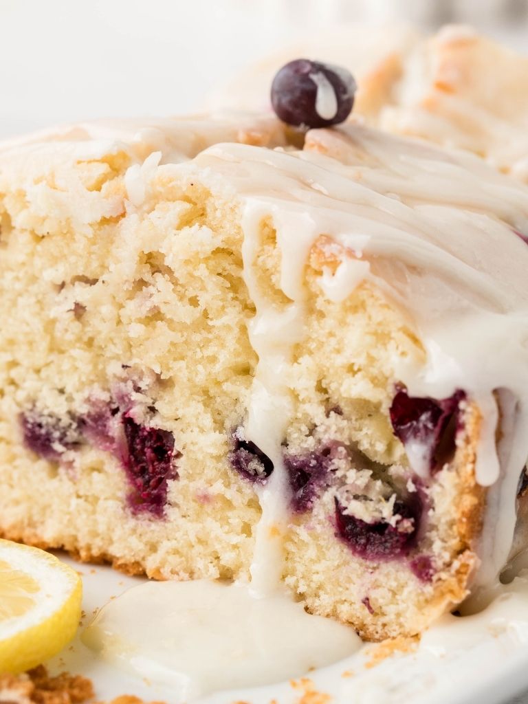 A loaf of lemon blueberry bread cut open to see the inside with some glaze over top of it. 