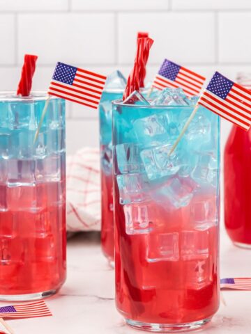 Glass cups with red, white, blue layers of drink with ice. Topped with licorice and an American flag for decoration.