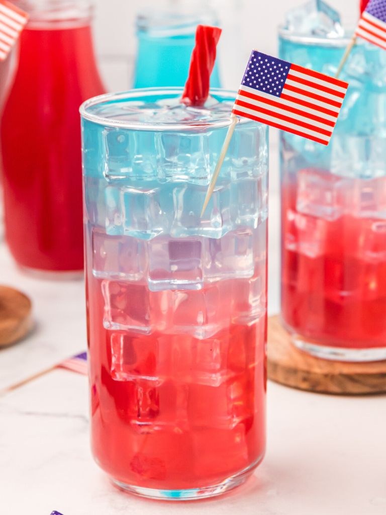 Layered red white blue drink inside a glass cup with ice cubes.