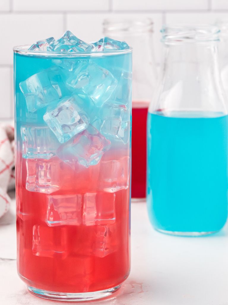 Glass cup with a layered drink for 4th of July with a bottle of blue juice beside it. 