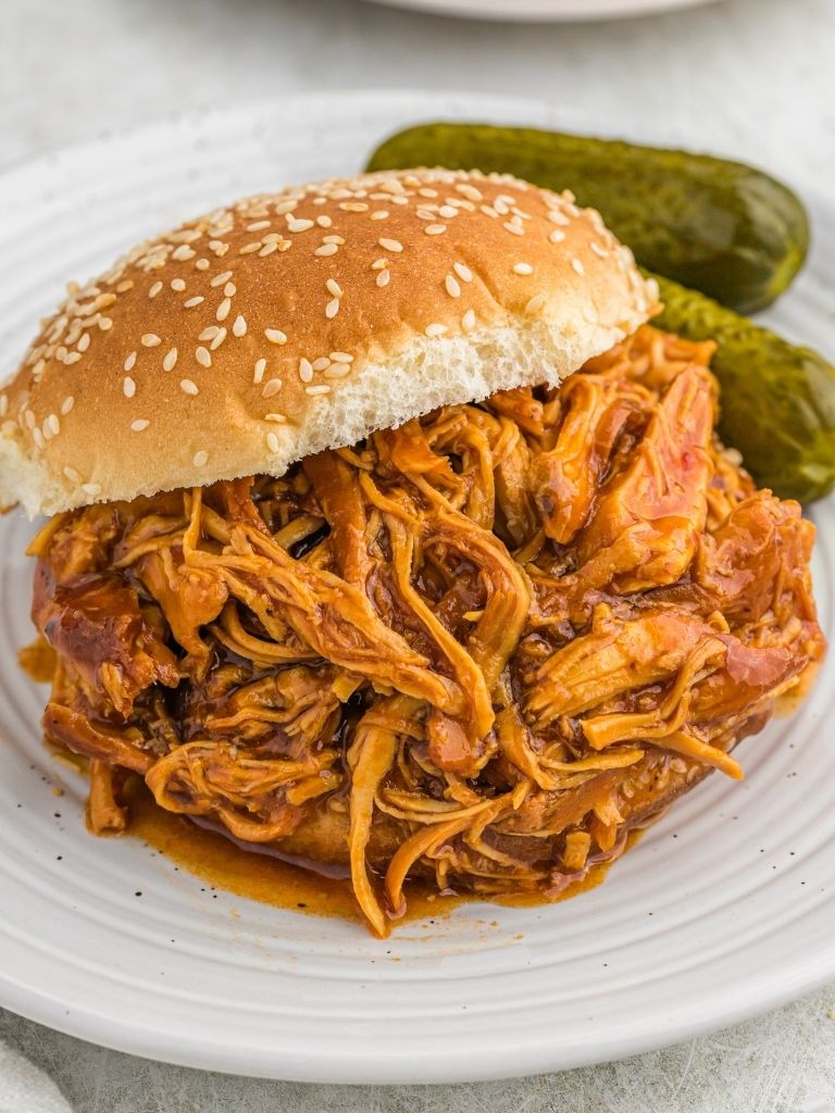 Shredded bbq chicken sandwich with pickles in the background.