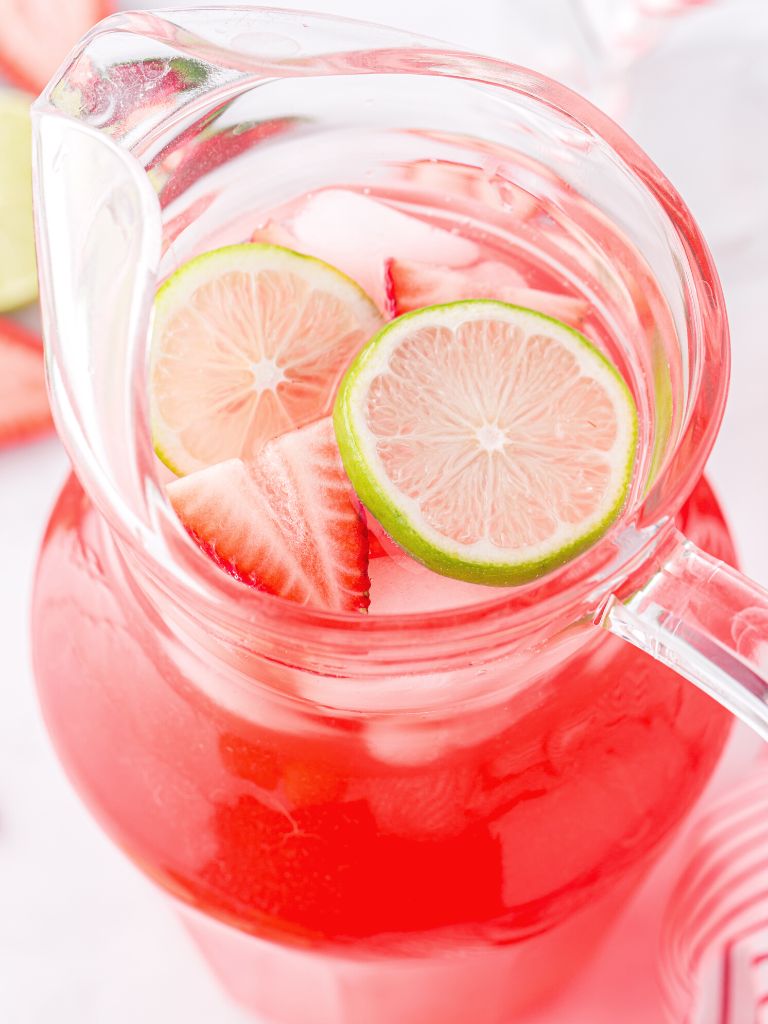 A glass pitcher of limeade with strawberries and lime slices on top. 