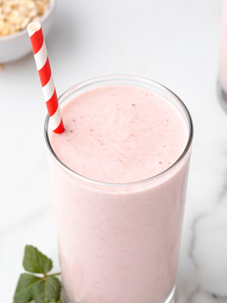 The top of a strawberry oat smoothie inside a glass cup with a red and white straw.