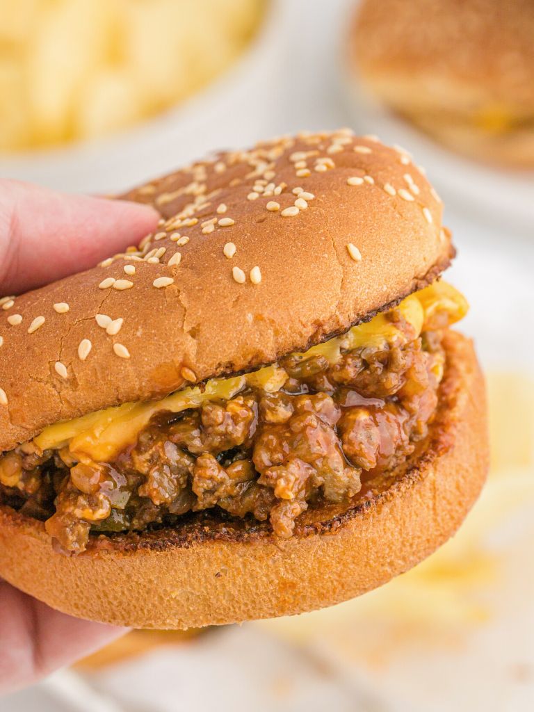 A hand holding a cheeseburger with ground beef on a hamburger bun. 