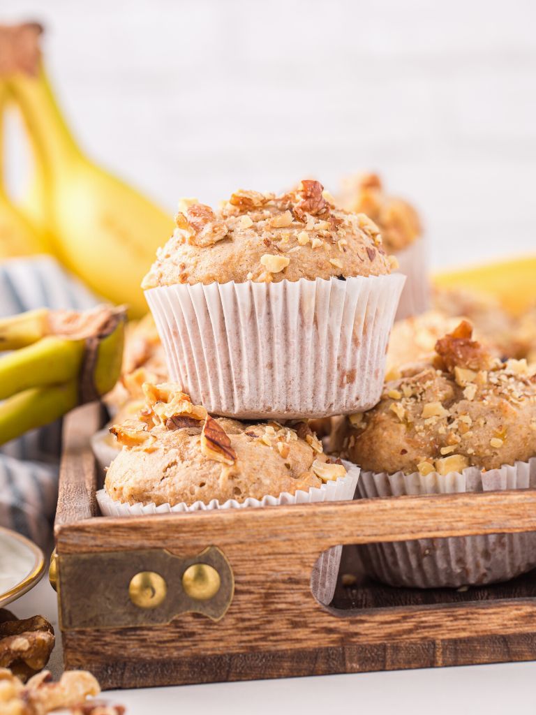 Muffins with bananas in the background on a wooden tray. 