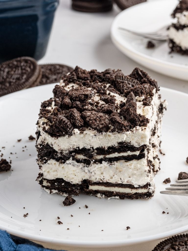 A square of icebox cake on a white plate with oreo cookies in the background.