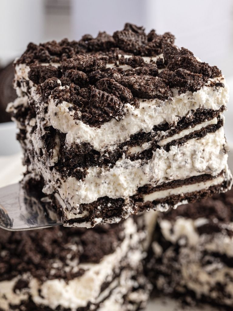 A spatula holding a piece of icebox cake on it over the pan of the cake below it. 