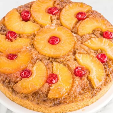 A pineapple upside down cake on top of a white pedestal plate.