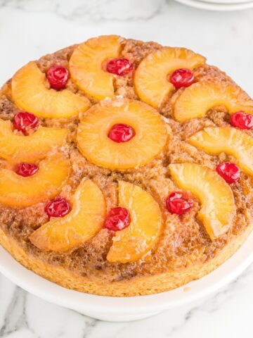 A pineapple upside down cake on top of a white pedestal plate.
