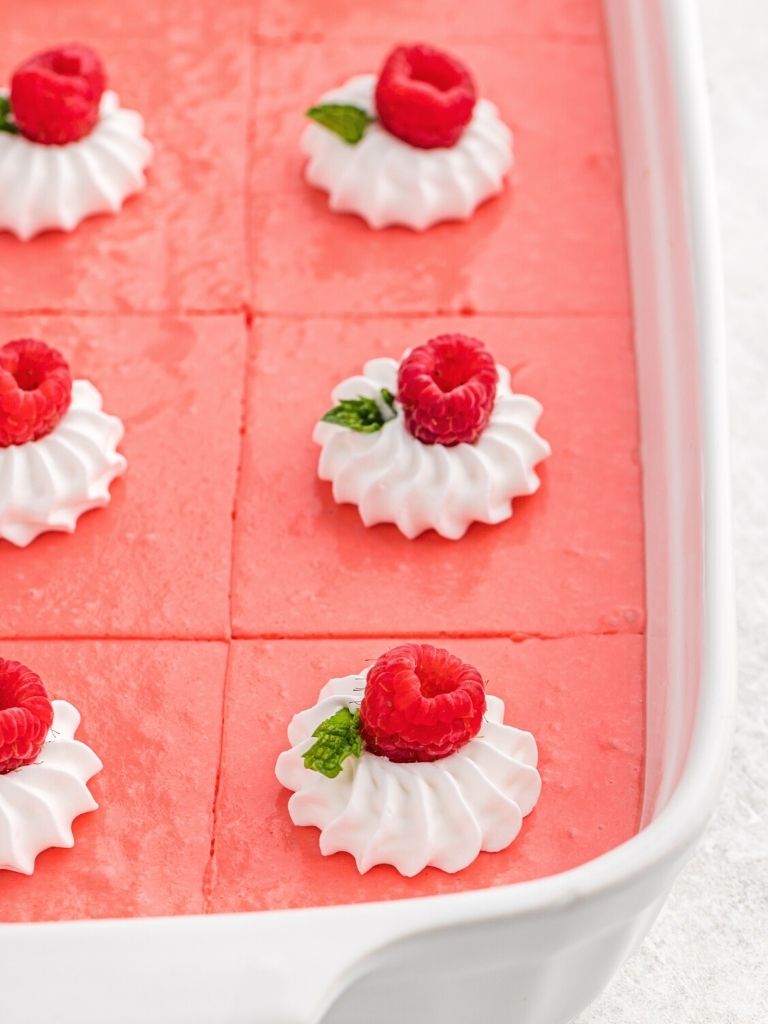A side view photo of a dish of jello topped with whipped cream and fresh raspberries. 