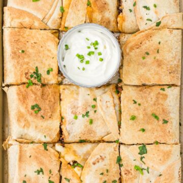 Overhead picture of a quesadilla in a sheet pan that's baked in the oven. With a bowl of sour cream next to it.