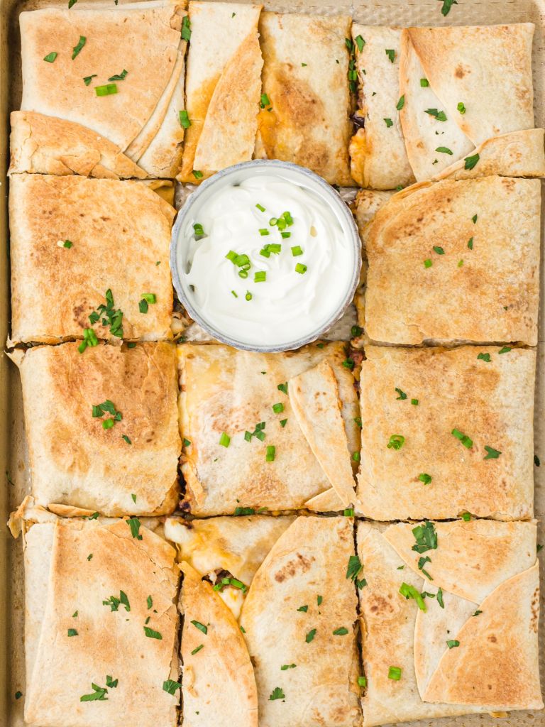 Overhead picture of a quesadilla in a sheet pan that's baked in the oven. With a bowl of sour cream next to it. 