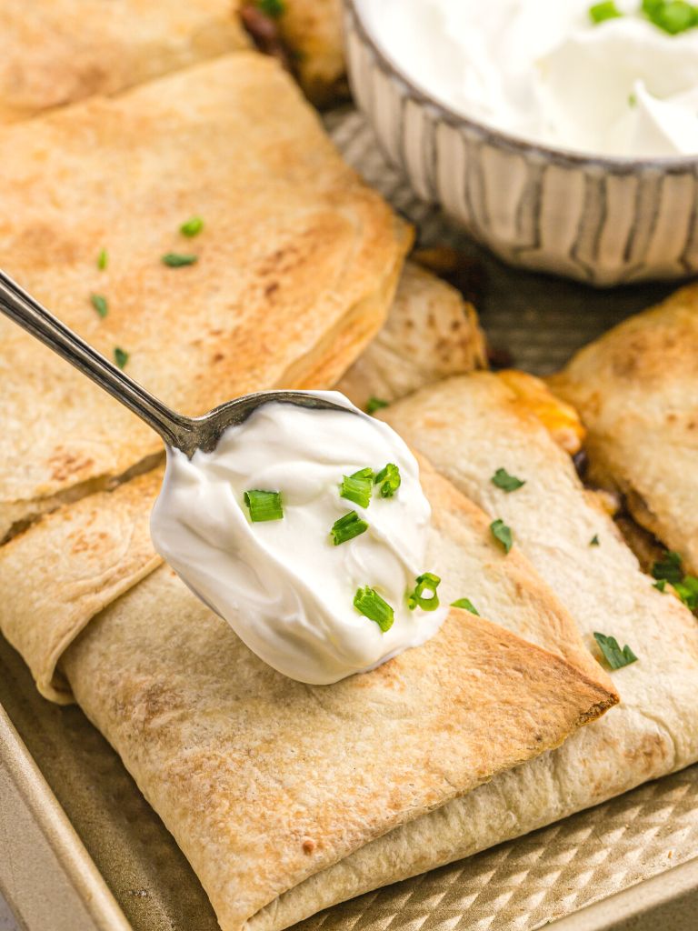 Quesadillas on a cookie sheet with a dollop of sour cream on one. 