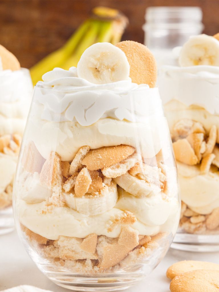 Glass cup with layers of pudding inside, banana slices, and Nilla Wafers. A wooden background with bananas.