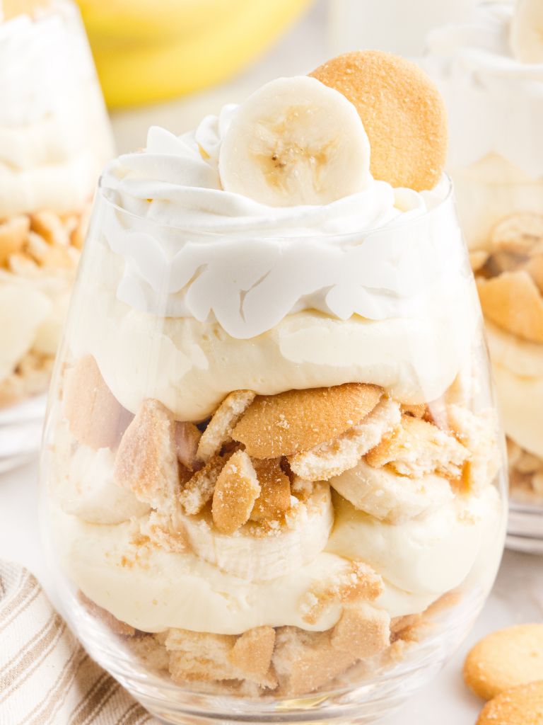Close up shot of a layered parfait topped with a banana slice and cookies on top. 