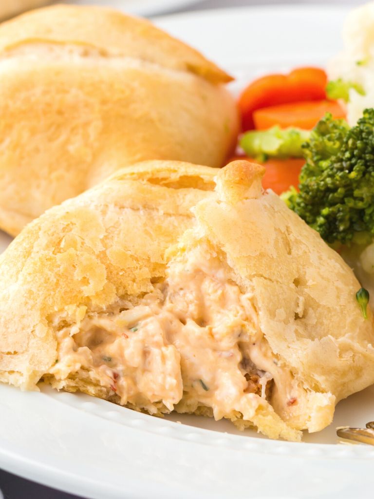 Close up photo of a chicken pillow made with buffalo chicken, opened up to show the creamy filling inside the crescent roll on a white plate.