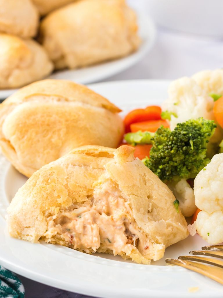 A dinner plate with vegetables, a fork, and a crescent chicken pillow on it. 
