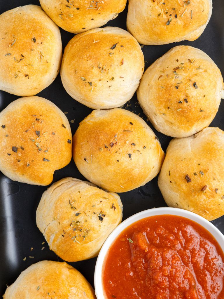 Biscuits stuffed with cheese on a black plate with a small bowl of marinara sauce in it. 
