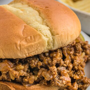 A hamburger bun with sloppy Joe meat inside of it on top of a gray plate.
