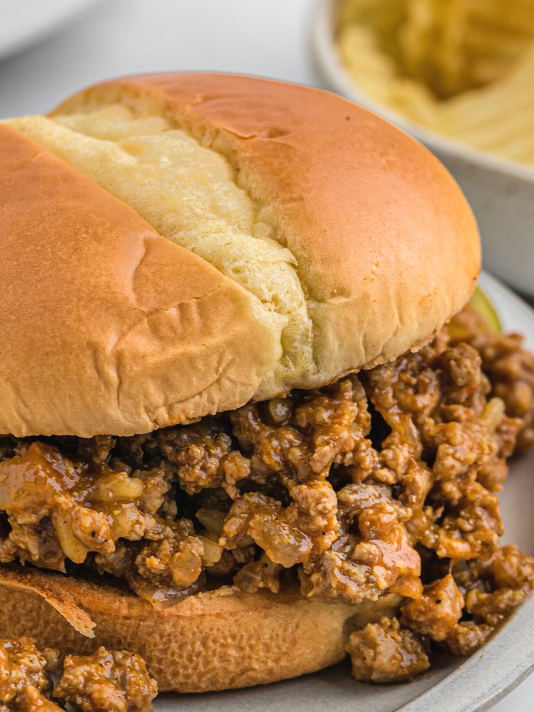 A hamburger bun with sloppy Joe meat inside of it on top of a gray plate. 