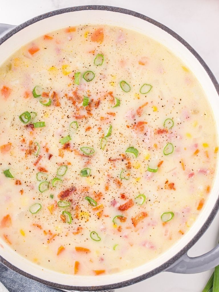 A pot of chowder, overhead picture of it, filled with vegetables like potato, corn, and ham. 